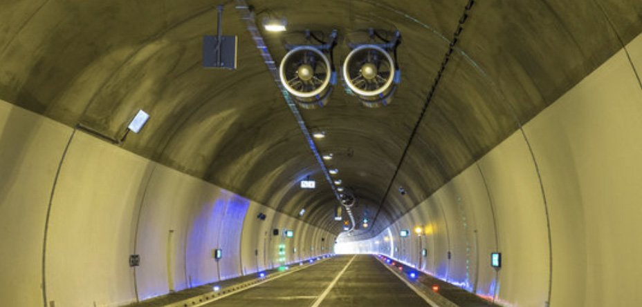 Two jet fans mounted on the ceiling of a concrete tunnel.