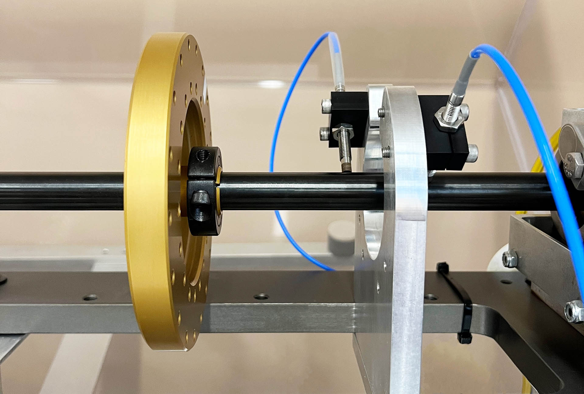 Two blue PRO Line proximity probes mounted using black mounting brackets to secure them above the rotating shaft of a machine with a gold gear.
