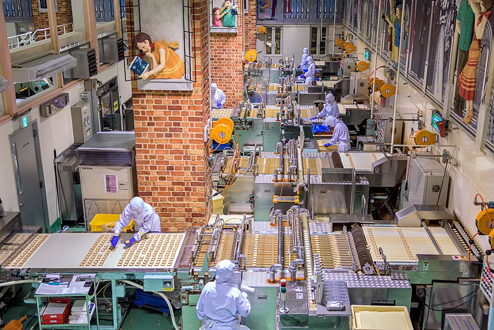 Workers in protective gear operating machinery on the floor of a chocolate manufacturing plant.